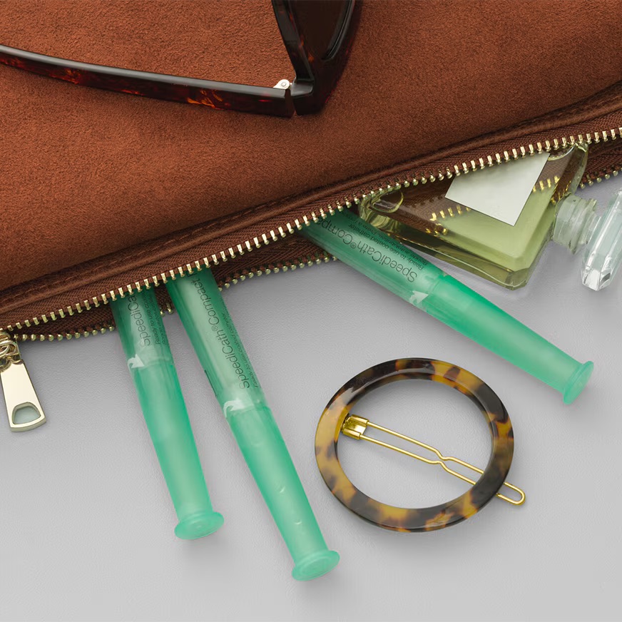 Les sondes speedicath compact pour femme rangés dans un sac à main avec un parfum et une barrette.